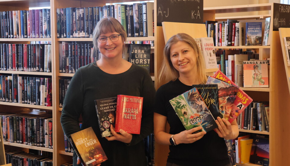Randi Heggland Strøm og Ieva Juceviciute-Ruse ved Tyrielden Eidskog bibliotek viser frem noen av de mest populære bøkene i 2024. Damer viser frem bøker i et bibliotek.
